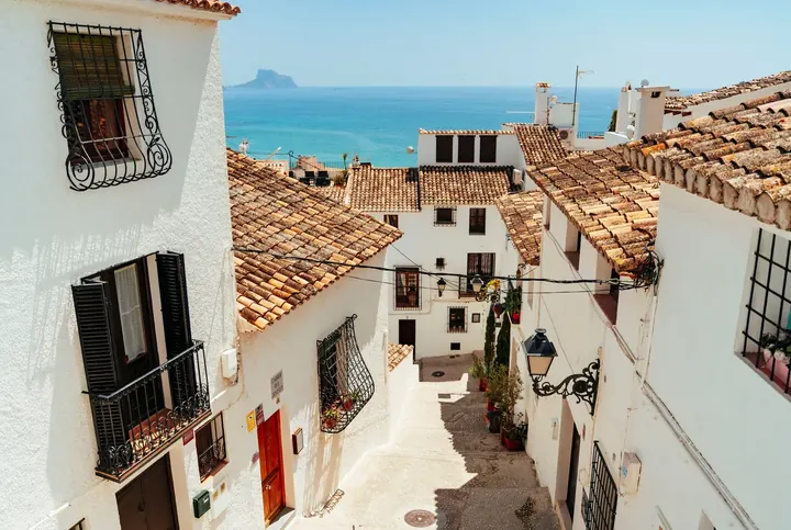Gasse mit weißen Häusern und Terrakottadächern, die zum Meer hinabführt, in Altea, Spanien